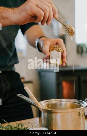 Ein Mann rührt Honig in einen Topf. Der Honig wird aus einem Glas in den Topf gegossen Stockfoto