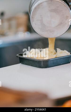 Ein Topf mit Lebensmitteln wird in ein Tablett gegossen. Das Essen ist gelb und sieht aus wie Kartoffelpüree Stockfoto