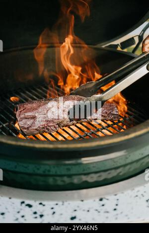 Eine Person kocht ein Steak auf einem Grill. Das Steak ist braun und hat viel Fett. Der Grill ist heiß und das Steak brodelt Stockfoto