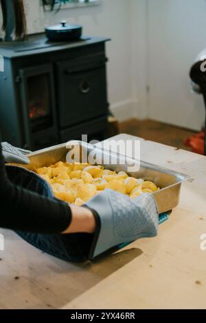 Eine Person kocht Kartoffeln in einer Pfanne auf einem Holztisch. Die Kartoffeln werden in kleine Stücke geschnitten und in einer Pfanne gekocht Stockfoto