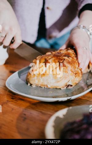 Eine Person schneidet ein Stück Fleisch auf einem Teller. Das Fleisch steht auf einem Holztisch Stockfoto