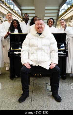 Tony Mortimer überrascht Pendler am St Pancras International Station in London mit einem Pop-up-Auftritt seiner Nummer eins zu Weihnachten 1994, „Stay Another Day“, unterstützt vom London Community Gospel Choir. Tony arbeitet mit der Musiktherapie-Wohltätigkeitsorganisation Nordoff und Robbins zusammen, um den 30. Jahrestag der Veröffentlichung des Songs zu feiern. Bilddatum: Freitag, 13. Dezember 2024. Stockfoto