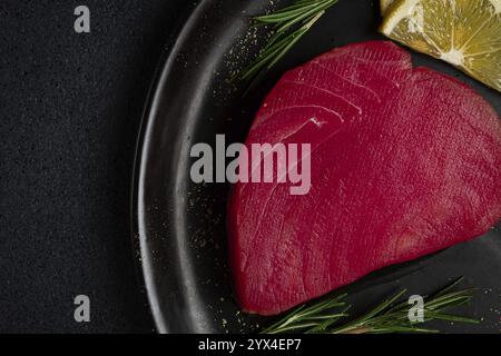 Frisches rotes Thunfischfilet, zum Steak, roh, von oben, auf einem schwarzen Teller, keine Leute Stockfoto