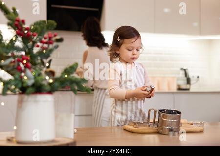 Süßes kleines Mädchen auf Schürze, das Kekse in der Küche backt, Weihnachtstraditionen Stockfoto