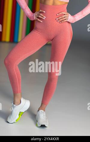 Seitenansicht einer sportlichen Frau mit rosafarbenen nahtlosen Leggings, passendem Oberteil und weißen Sneakers, die in einer farbenfrohen Umgebung posiert. Stockfoto