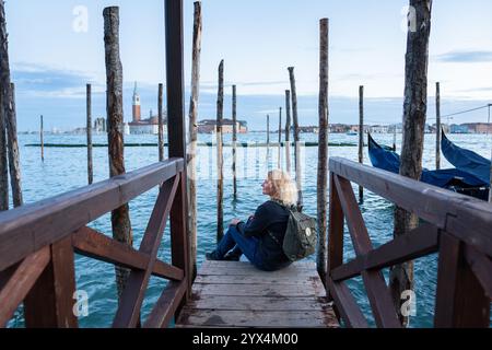 Junge blonde Frau, die vom Gondelpier in Venedig, Italien, den Blick über die venezianische Lagune genießt. Stockfoto