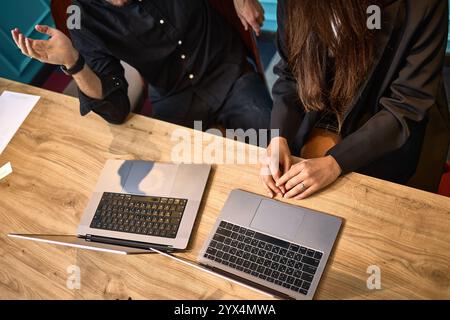 Zwei Kollegen arbeiten in einer modernen Büroumgebung zusammen und diskutieren ein Projekt mit Laptops auf einem Holztisch, professionelles Teamwork-Konzept Stockfoto