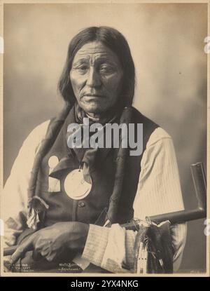 Weißer Büffel, von den Arapaho-Leuten, 1898. Studio-Porträt eines Ureinwohner-Mannes mit Stoffflechten, Westernhemd, Westernweste, Taschentuch und Friedensmedaille und Pfeife. Stockfoto
