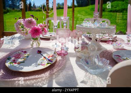 Elegante rosafarbene und weiße Tischdekoration mit Blumen und Kerzen in einem wunderschönen Wintergarten. Stockfoto