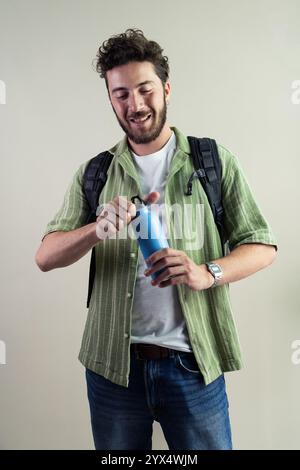 Authentisches Porträt eines glücklichen jungen Schülers mit wiederverwendbarer Wasserflasche und Rucksack. Ein natürliches Lifestyle-Bild, das eine nachhaltige und umweltfreundliche Wahl darstellt Stockfoto