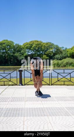 Fitter junger Mann, der sich nach dem Workout an einem ruhigen See im Stadtpark ausdehnt. Stockfoto