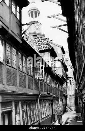 Ein Mann läuft entlang der engen Straße entlang der Kramer Amtsstuben auf Krayenkamp. Der Turm von St. Michael ist im Hintergrund zu sehen. [Automatisierte Übersetzung] Stockfoto