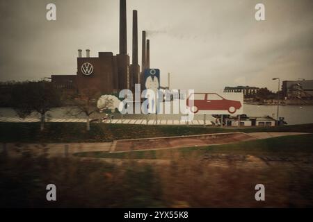 Wolfsburg, Deutschland. November 2024. Das KWK-Kraftwerk Wolfsburg Nord/Süd, auch als altes KWK-Kraftwerk bekannt, mit dem VW-Logo auf dem Gelände des Volkswagen-Werks, fotografiert durch das Fenster eines fahrenden Zuges über den Mittellandkanal. Teile der Autostadt sind auf der rechten Seite zu sehen. Quelle: Stefan Jaitner/dpa/Alamy Live News Stockfoto