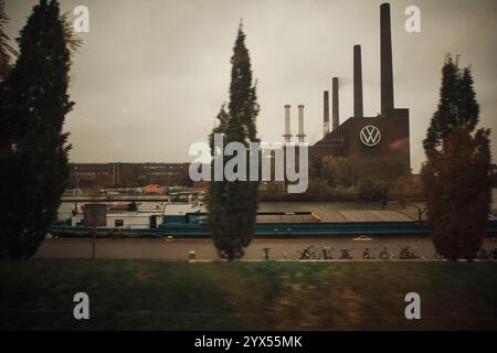 Wolfsburg, Deutschland. November 2024. Das KWK-Kraftwerk Wolfsburg Nord/Süd, auch als altes KWK-Kraftwerk bekannt, mit dem VW-Logo auf dem Gelände des Volkswagen-Werks, fotografiert durch das Fenster eines fahrenden Zuges über den Mittellandkanal. Quelle: Stefan Jaitner/dpa/Alamy Live News Stockfoto