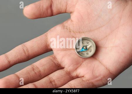Nahaufnahme der Hand mit kleinem runden Vintage Taschenkompass isolierter grauer Hintergrund, weißes Zifferblatt mit Markierungen für Kardinalrichtungen und -Punkte Stockfoto