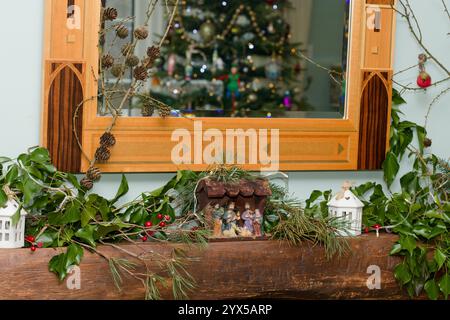 Eine Krippe auf einem Kaminsims. Feenlichter und dekoratives Laub mit einem spiegelreflektierenden Baum. Weihnachtsdekoration in einem Haus in England, Großbritannien. Stockfoto