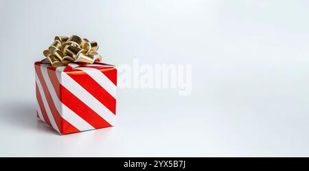 Geschenkbox aus rot-weiß gestreiftem Papier mit goldener Schleife und Kopierraum. Stockfoto