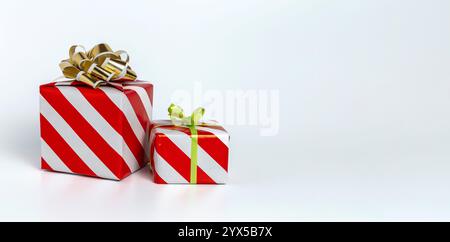 Zwei Geschenke in gestreiftes rot-weißes Geschenkpapier mit goldener Schleife und grünem Band. Kopierbereich. Stockfoto