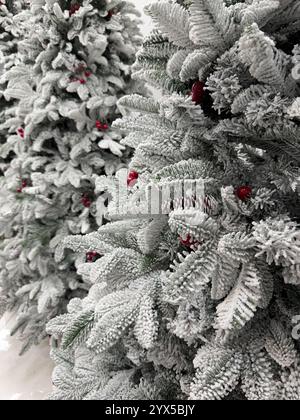 Dieses Foto am Tag zeigt eine Nahaufnahme von schneebedeckten künstlichen Weihnachtsbäumen, deren Zweige mit leuchtenden roten Beeren geschmückt sind. Die mattierte n Stockfoto