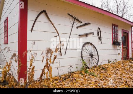Weiße und rote hölzerne rustikale Tafel Garage und Gartenschuppen dekoriert mit alten Handwerkzeugen, Wagenrad und gefallenen Blättern im Herbst. Stockfoto