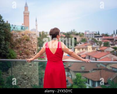 Frau in rotem Kleid, die in den engen Gassen der Altstadt von Antalya während des warmen Sommerabends spaziert. Historische Atmosphäre und mediterraner Charme sorgen für Ruhe Stockfoto