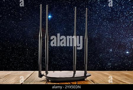 Ein Router für die WLAN-Verteilung auf einem Holztisch, Nahaufnahme, vor dem Hintergrund eines Sternenhimmels. Stockfoto