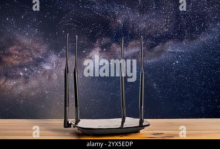 Ein Router für die WLAN-Verteilung auf einem Holztisch, Nahaufnahme, vor dem Hintergrund eines Sternenhimmels. Stockfoto