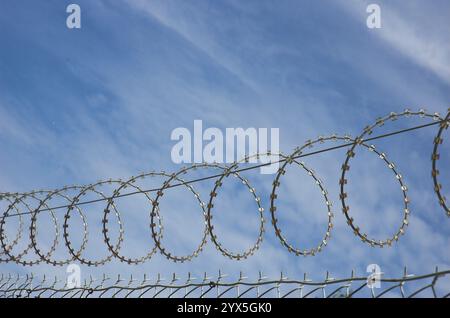 Stacheldraht, der an der Oberseite eines Zauns um einen sicheren, eingeschränkten Zugangsbereich gewickelt ist. Stockfoto