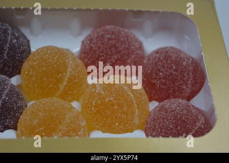 Originale finnische Gelee-Bonbons in Form von runden Kugeln, die mit weißem Zucker bedeckt sind. Gelbe, orange, kirschrote, gummiartige Bonbons sind in weißer Verpackung. Stockfoto