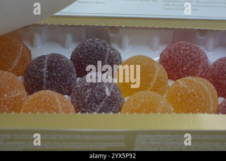 Originale finnische Gelee-Bonbons in Form von runden Kugeln, die mit weißem Zucker bedeckt sind. Gelbe, orange, kirschrote, gummiartige Bonbons sind in weißer Verpackung. Stockfoto