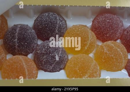 Originale finnische Gelee-Bonbons in Form von runden Kugeln, die mit weißem Zucker bedeckt sind. Gelbe, orange, kirschrote, gummiartige Bonbons sind in weißer Verpackung. Stockfoto