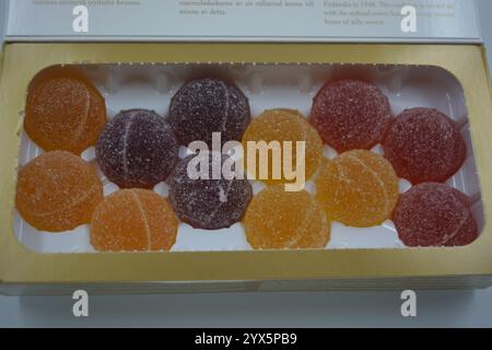 Originale finnische Gelee-Bonbons in Form von runden Kugeln, die mit weißem Zucker bedeckt sind. Gelbe, orange, kirschrote, gummiartige Bonbons sind in weißer Verpackung. Stockfoto