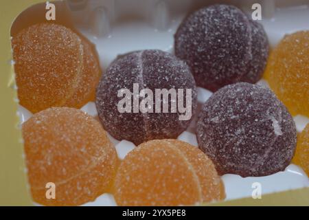 Originale finnische Gelee-Bonbons in Form von runden Kugeln, die mit weißem Zucker bedeckt sind. Gelbe, orange, kirschrote, gummiartige Bonbons sind in weißer Verpackung. Stockfoto