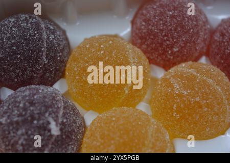 Originale finnische Gelee-Bonbons in Form von runden Kugeln, die mit weißem Zucker bedeckt sind. Gelbe, orange, kirschrote, gummiartige Bonbons sind in weißer Verpackung. Stockfoto