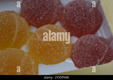 Originale finnische Gelee-Bonbons in Form von runden Kugeln, die mit weißem Zucker bedeckt sind. Gelbe, orange, kirschrote, gummiartige Bonbons sind in weißer Verpackung. Stockfoto