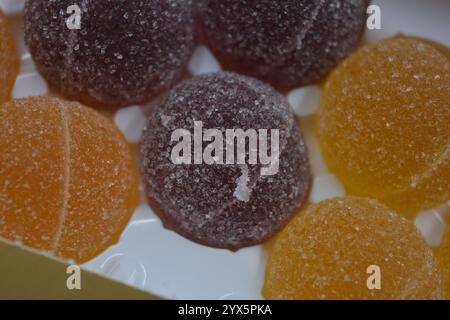Originale finnische Gelee-Bonbons in Form von runden Kugeln, die mit weißem Zucker bedeckt sind. Gelbe, orange, kirschrote, gummiartige Bonbons sind in weißer Verpackung. Stockfoto