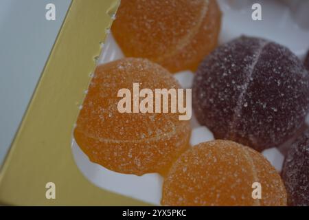 Originale finnische Gelee-Bonbons in Form von runden Kugeln, die mit weißem Zucker bedeckt sind. Gelbe, orange, kirschrote, gummiartige Bonbons sind in weißer Verpackung. Stockfoto