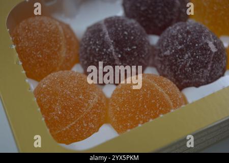 Originale finnische Gelee-Bonbons in Form von runden Kugeln, die mit weißem Zucker bedeckt sind. Gelbe, orange, kirschrote, gummiartige Bonbons sind in weißer Verpackung. Stockfoto