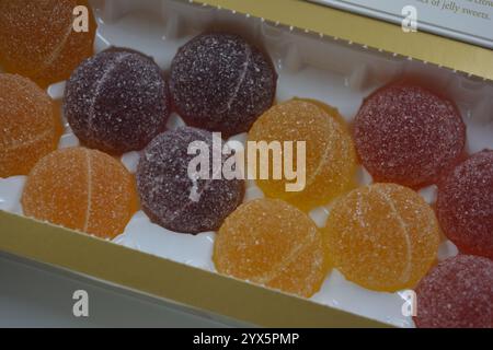 Originale finnische Gelee-Bonbons in Form von runden Kugeln, die mit weißem Zucker bedeckt sind. Gelbe, orange, kirschrote, gummiartige Bonbons sind in weißer Verpackung. Stockfoto