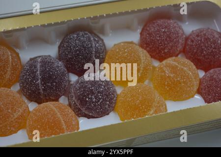 Originale finnische Gelee-Bonbons in Form von runden Kugeln, die mit weißem Zucker bedeckt sind. Gelbe, orange, kirschrote, gummiartige Bonbons sind in weißer Verpackung. Stockfoto
