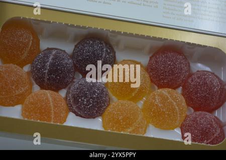 Originale finnische Gelee-Bonbons in Form von runden Kugeln, die mit weißem Zucker bedeckt sind. Gelbe, orange, kirschrote, gummiartige Bonbons sind in weißer Verpackung. Stockfoto