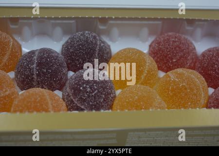 Originale finnische Gelee-Bonbons in Form von runden Kugeln, die mit weißem Zucker bedeckt sind. Gelbe, orange, kirschrote, gummiartige Bonbons sind in weißer Verpackung. Stockfoto