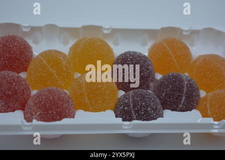 Originale finnische Gelee-Bonbons in Form von runden Kugeln, die mit weißem Zucker bedeckt sind. Gelbe, orange, kirschrote, gummiartige Bonbons sind in weißer Verpackung. Stockfoto