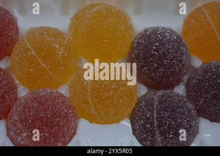Originale finnische Gelee-Bonbons in Form von runden Kugeln, die mit weißem Zucker bedeckt sind. Gelbe, orange, kirschrote, gummiartige Bonbons sind in weißer Verpackung. Stockfoto