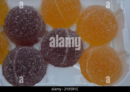 Originale finnische Gelee-Bonbons in Form von runden Kugeln, die mit weißem Zucker bedeckt sind. Gelbe, orange, kirschrote, gummiartige Bonbons sind in weißer Verpackung. Stockfoto