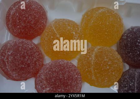 Originale finnische Gelee-Bonbons in Form von runden Kugeln, die mit weißem Zucker bedeckt sind. Gelbe, orange, kirschrote, gummiartige Bonbons sind in weißer Verpackung. Stockfoto