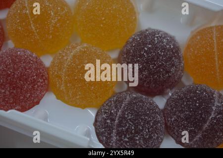 Originale finnische Gelee-Bonbons in Form von runden Kugeln, die mit weißem Zucker bedeckt sind. Gelbe, orange, kirschrote, gummiartige Bonbons sind in weißer Verpackung. Stockfoto