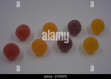 Originale finnische Gelee-Bonbons in Form von runden Kugeln, die mit weißem Zucker bedeckt sind. Gelbe, orange, kirschrote, gummirote Bonbons sind auf einem weißen Plastik. Stockfoto