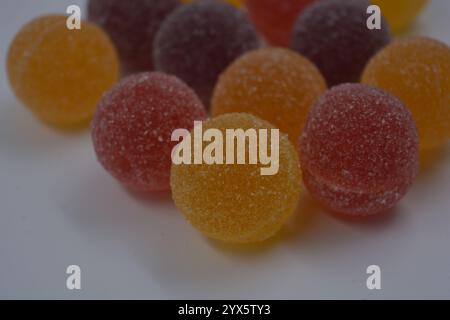 Originale finnische Gelee-Bonbons in Form von runden Kugeln, die mit weißem Zucker bedeckt sind. Gelbe, orange, kirschrote, gummirote Bonbons sind auf einem weißen Plastik. Stockfoto