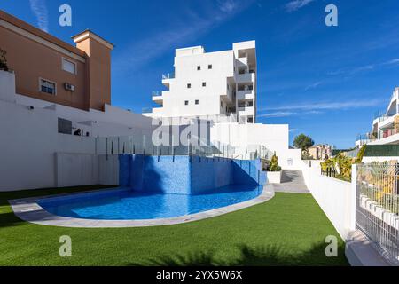 Ein stilvoller Wohnkomplex mit einem geschwungenen Pool mit blauen Fliesen, Kunstrasen und moderner Architektur unter sonnigem Himmel. Stockfoto